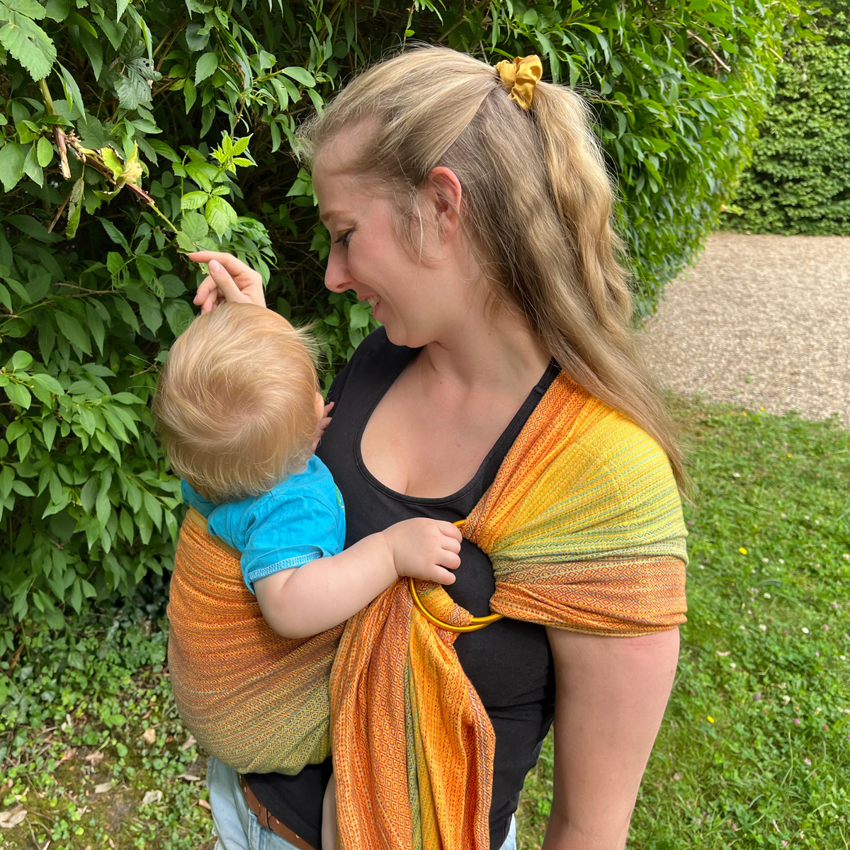 Ringsling Free Elf fusion d&#39;oro double weft Tragebild mit Baby und Mama vor einer grünen Hecke